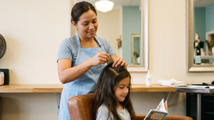 Trained lice-removal technician gently sectioning a child's long hair in a calm Mercer County salon chair with a fine metal nit comb under soft overhead light