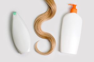 Shampoo and conditioner bottles next to a lock of blonde hair on a light background