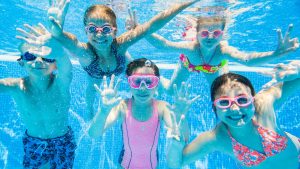 Children swimming underwater in a community pool, illustrating the question of whether chlorinated pool water kills head lice.