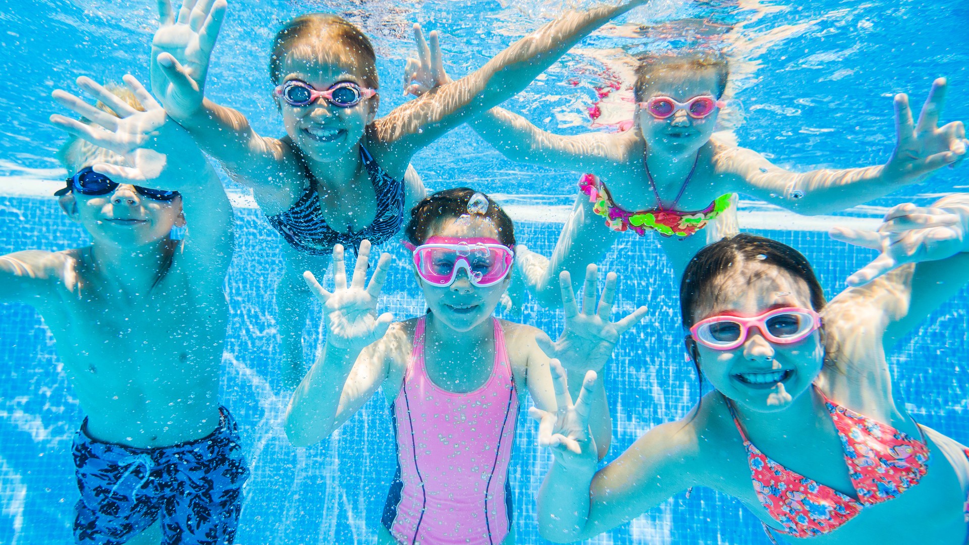 Children swimming underwater in a community pool, illustrating the question of whether chlorinated pool water kills head lice.
