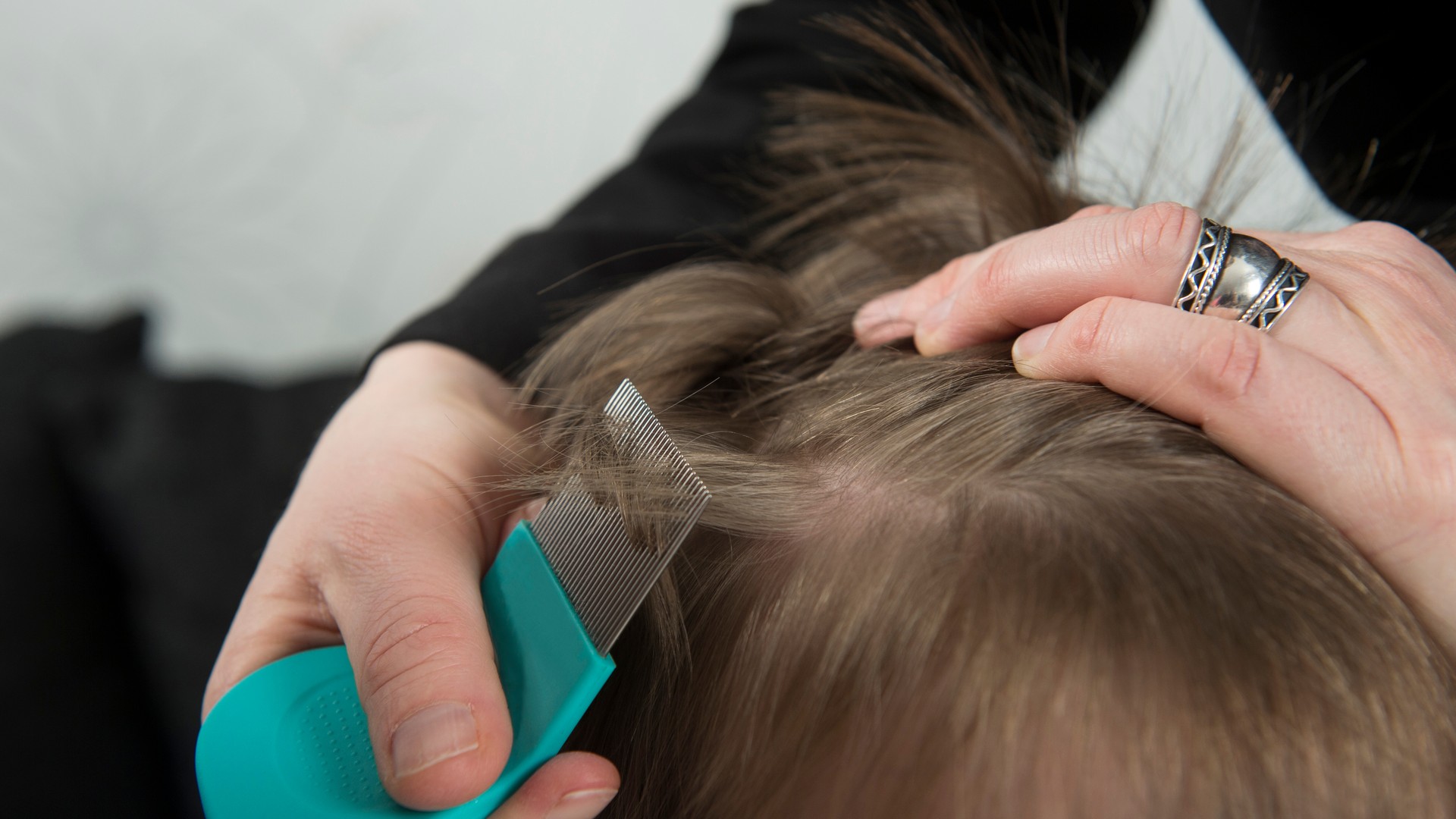 Bottle of isopropyl rubbing alcohol next to a fine-toothed metal lice comb on a bathroom counter, representing the DIY rubbing alcohol question parents weigh after a head lice diagnosis.