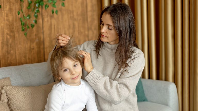 Adult separating a child's hair near the scalp while seated on a sofa