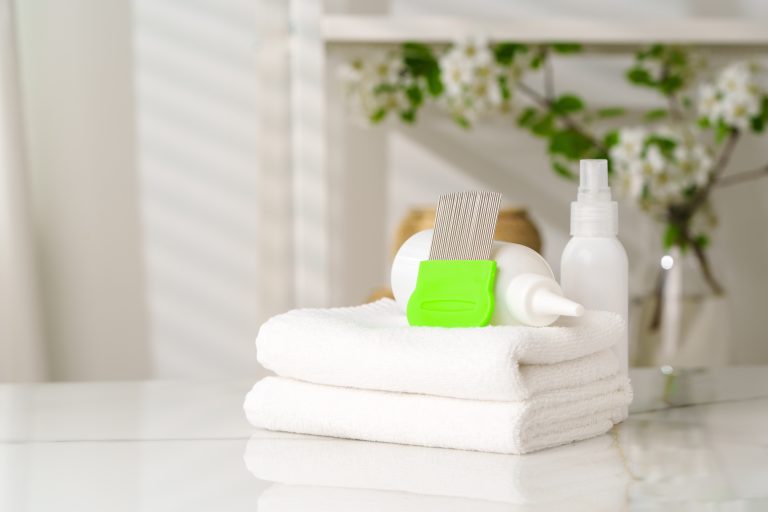 Green-handled fine-toothed comb and white bottles arranged on folded white towels.