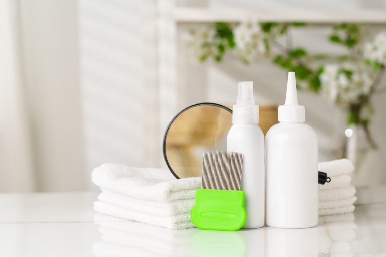 Green fine-tooth comb beside white bottles, folded towels and a mirror