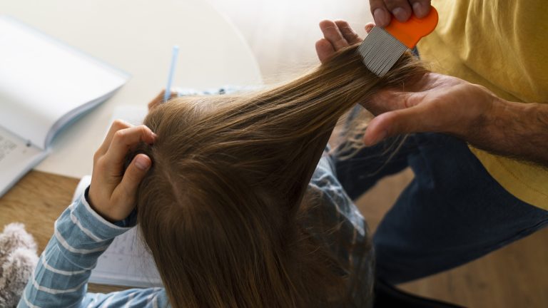 Adult combing a lifted section of long hair with an orange-handled fine-tooth comb