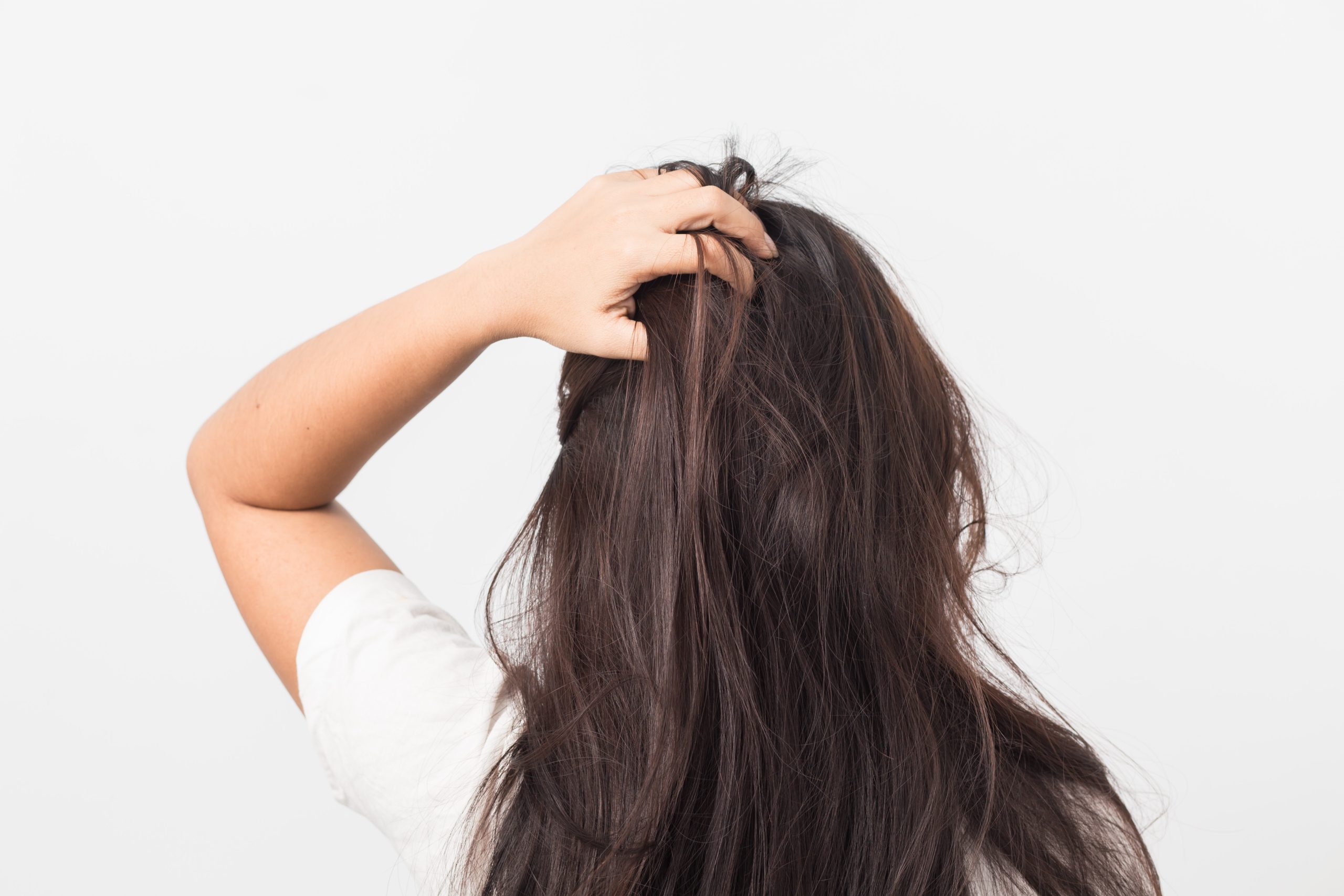 Back view of a woman with long dark hair raising one hand into her hair to scratch her scalp