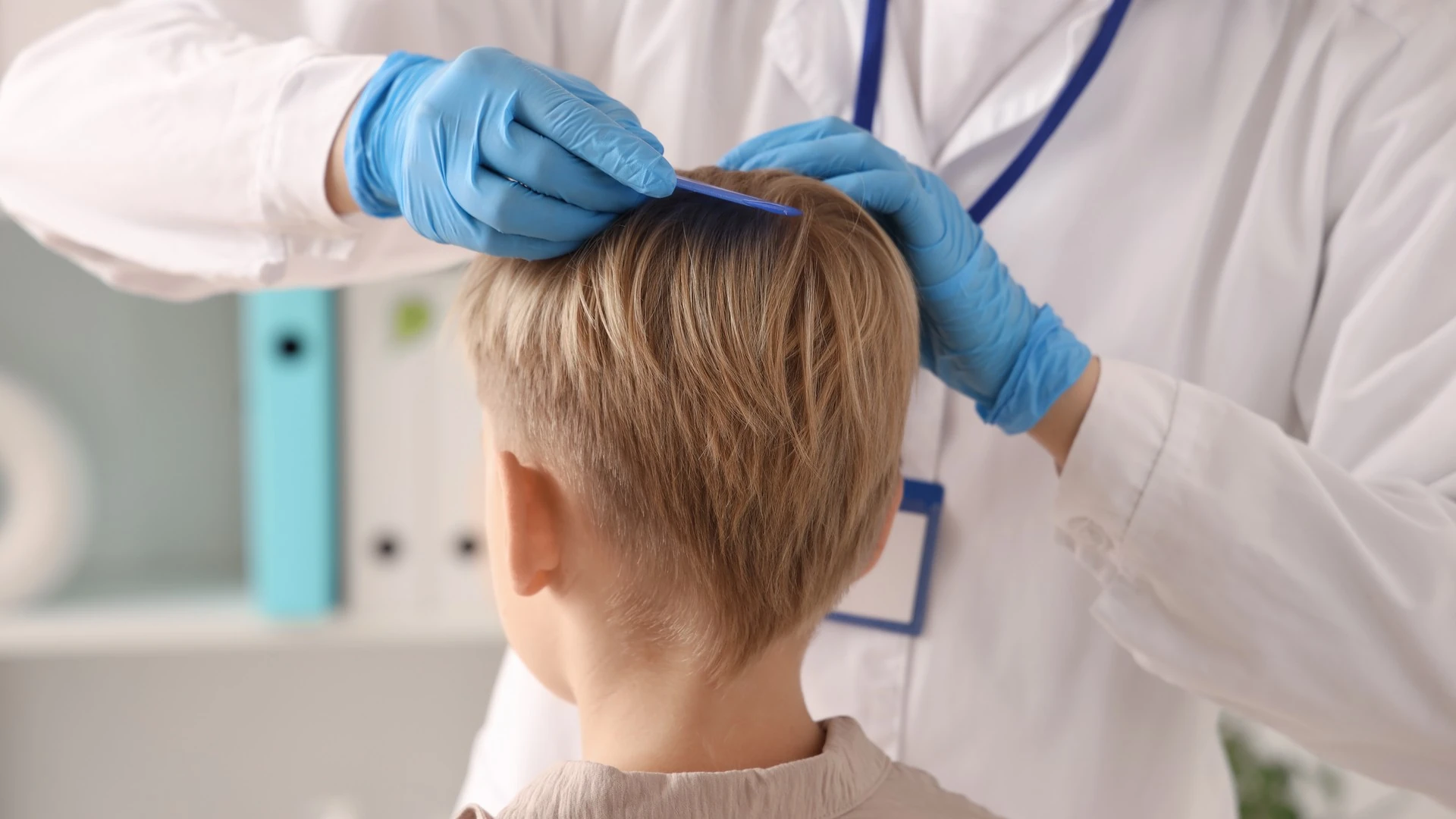 Blue-gloved hands combing a child's short hair at the crown