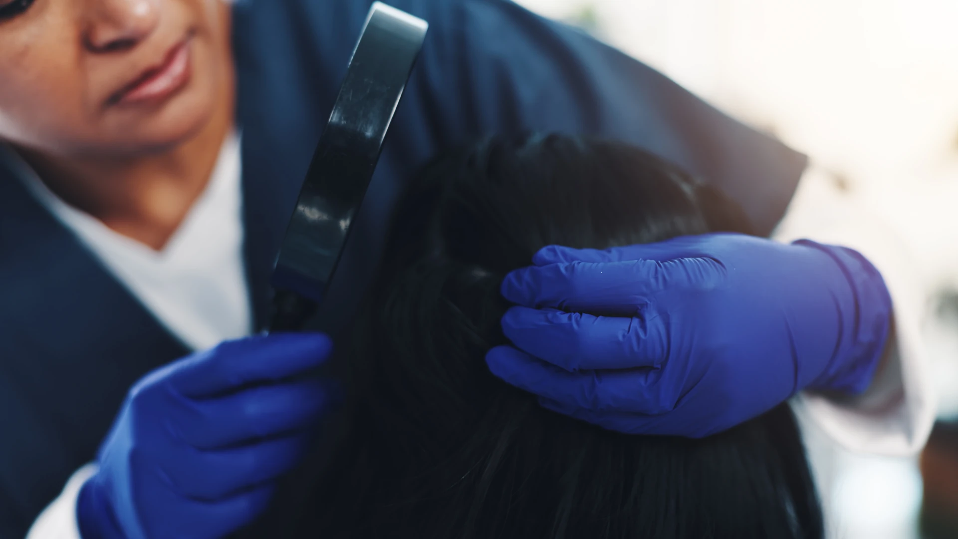 Adult wearing gloves examining dark hair with a magnifying glass